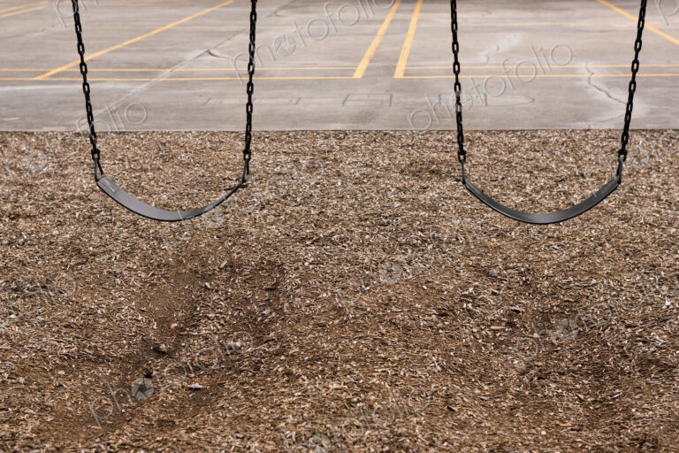 Playground swings, two empty children's swings, above a bark base.