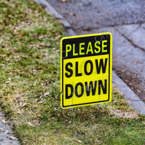 Please Slow Down sign on lawn between a sidewalk and the street