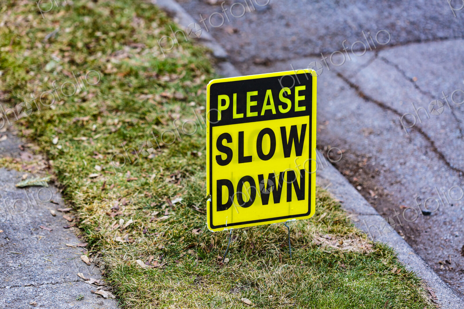 Please Slow Down sign on lawn between a sidewalk and the street