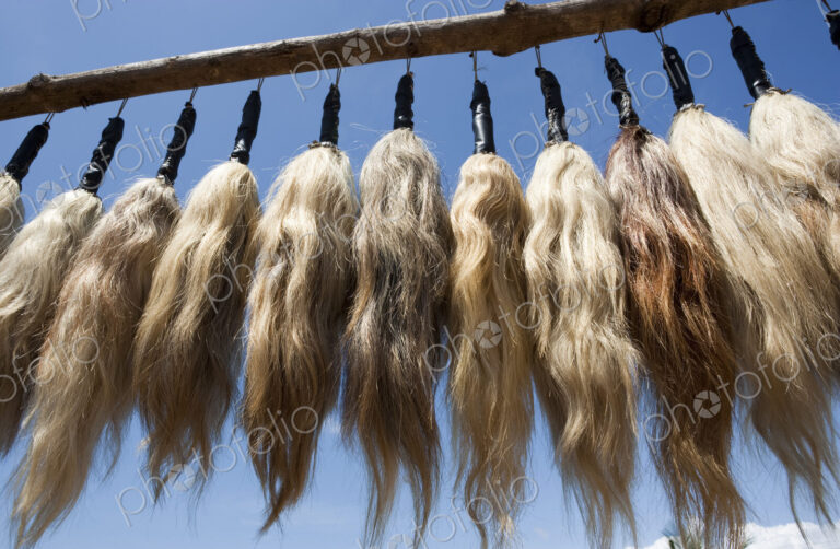 Plumes of human hair hanging from a frame against a blue sky.
