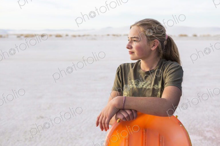 Portrait of 13 year old girl leaning on orange sled, White Sands Nat'l Monument, NM