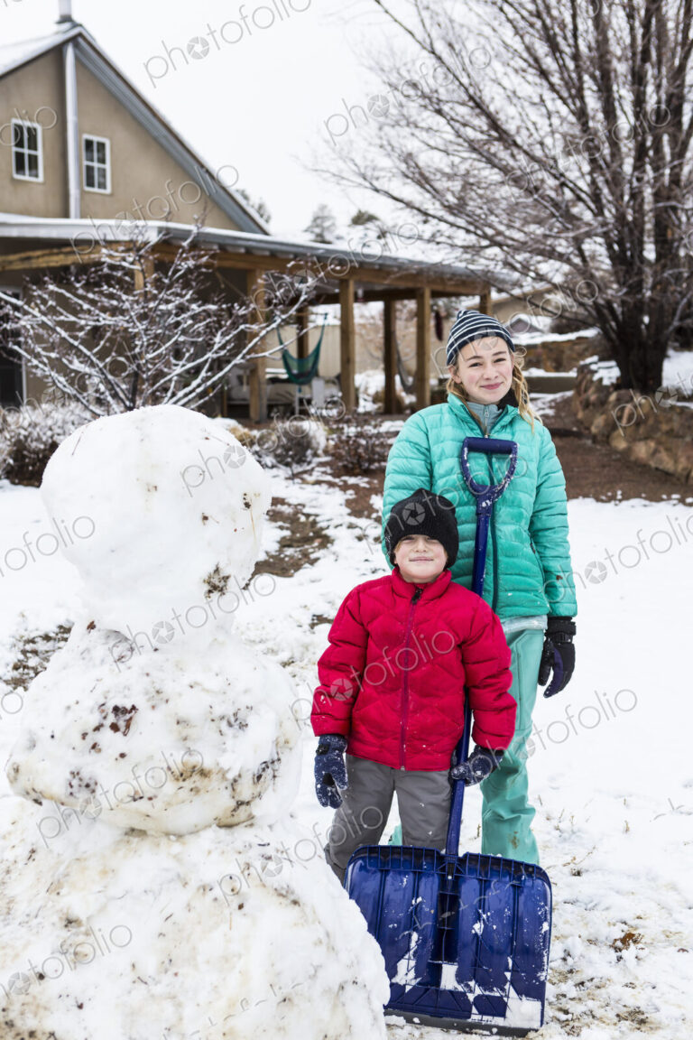 Portrait of Thirteen year old teenage girl and her 6 year old brother posing with snowman