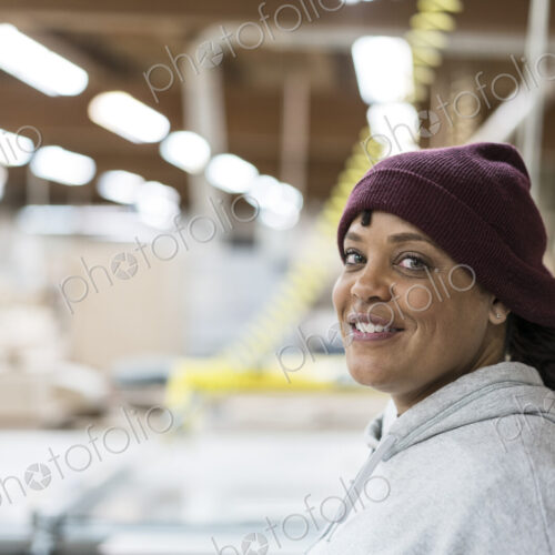 Portrait of a Black woman carpenter in a large woodworking shop.