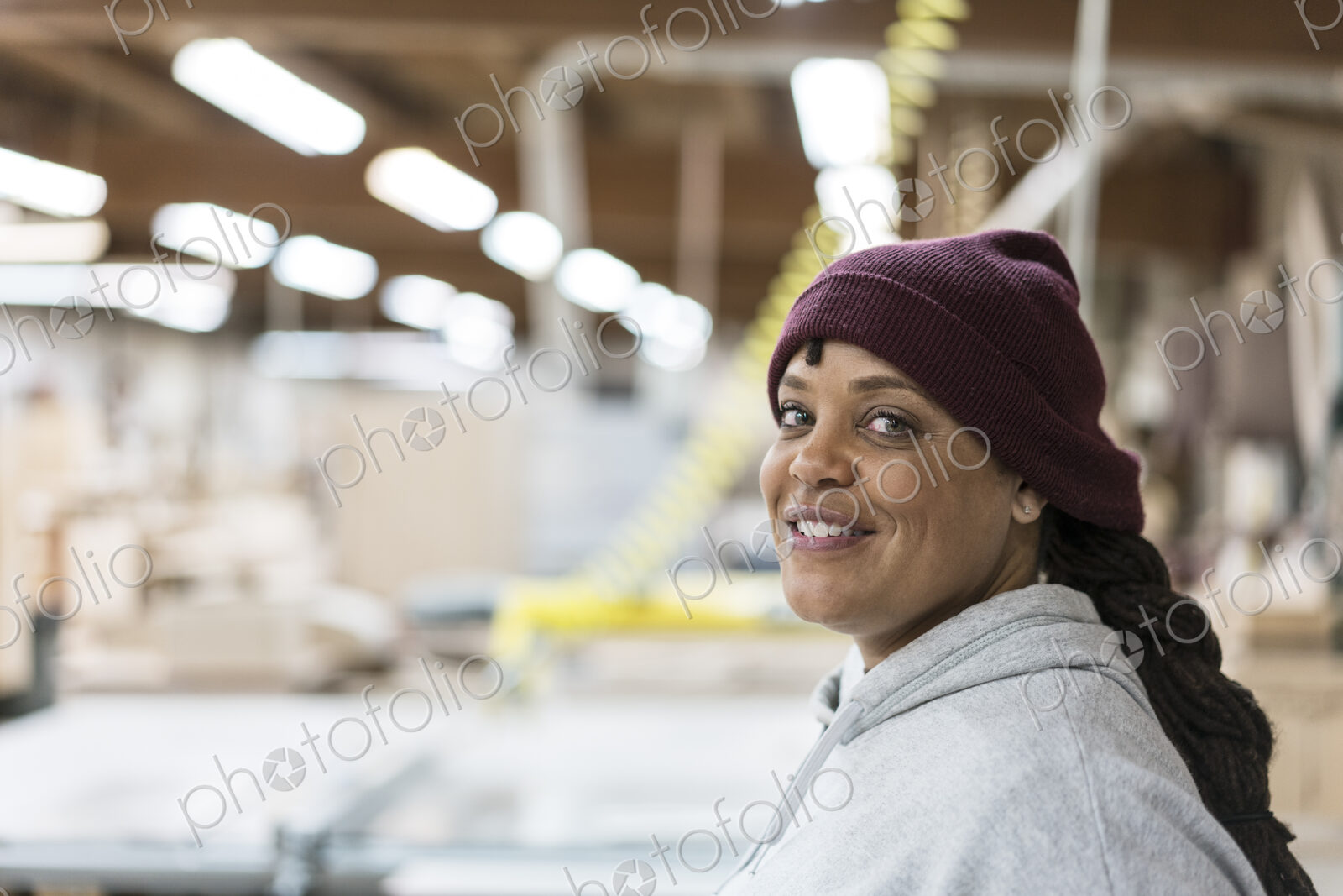Portrait of a Black woman carpenter in a large woodworking shop.