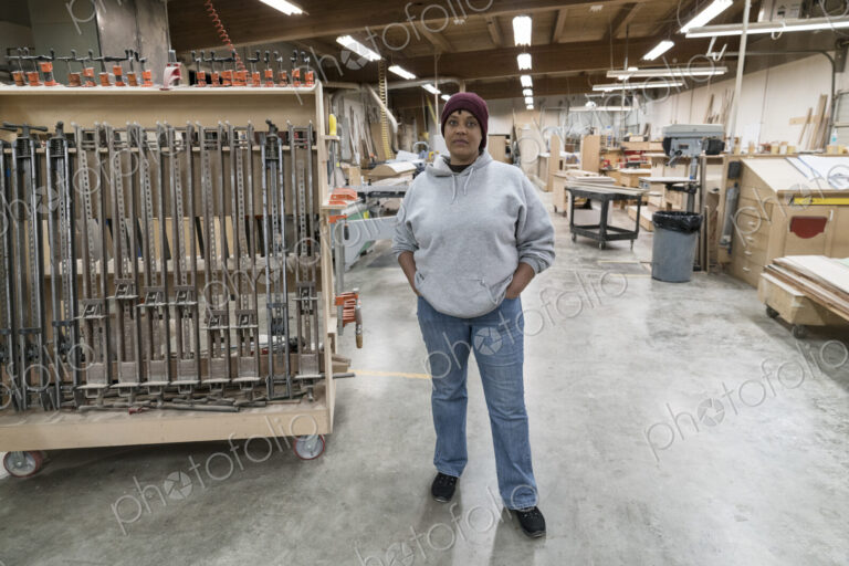 Portrait of a Black woman carpenter in a large woodworking shop.