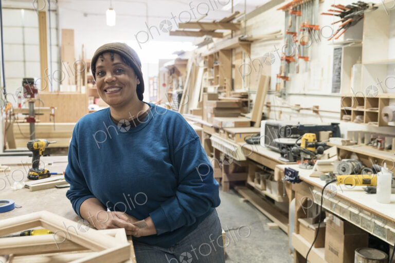 Portrait of a Black woman carpenter in a large woodworking shop.