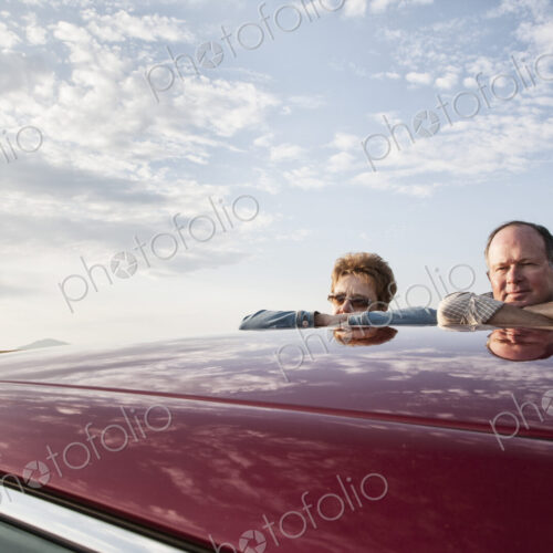 Portrait of a Caucasian senior couple leaning on their car at a rest stop on a road trip.