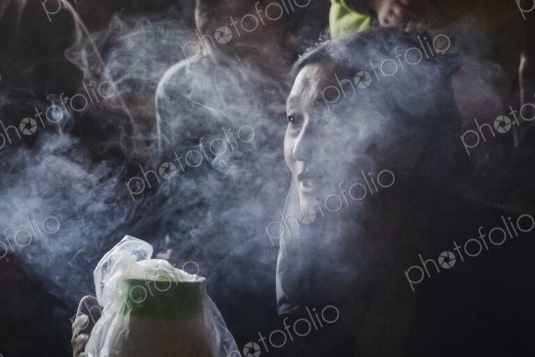 Portrait of a Tibetan Woman in a monastery, face wreathed in smoke.