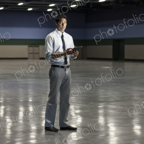 Portrait of a businessman holding a notebook computer and standing in a dimly lit and… Portrait of a businessman holding a notebook computer and standing in a dimly lit and…