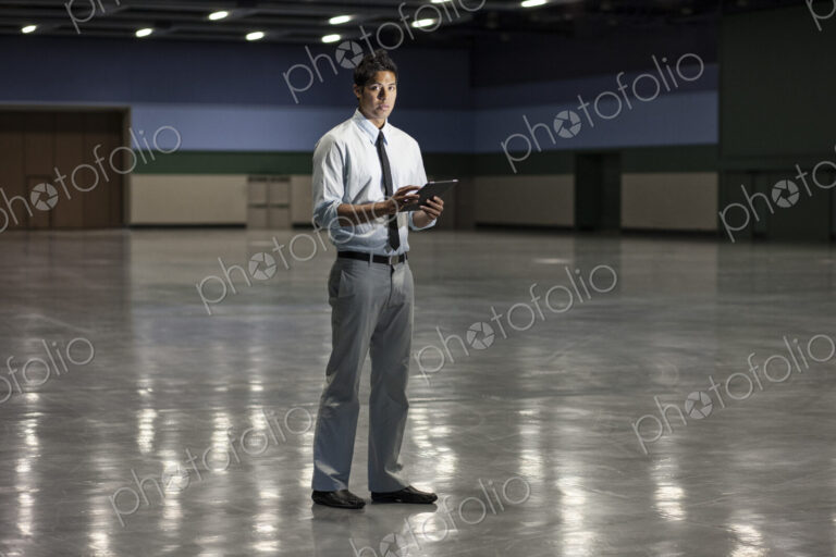 Portrait of a businessman holding a notebook computer and standing in a dimly lit and…