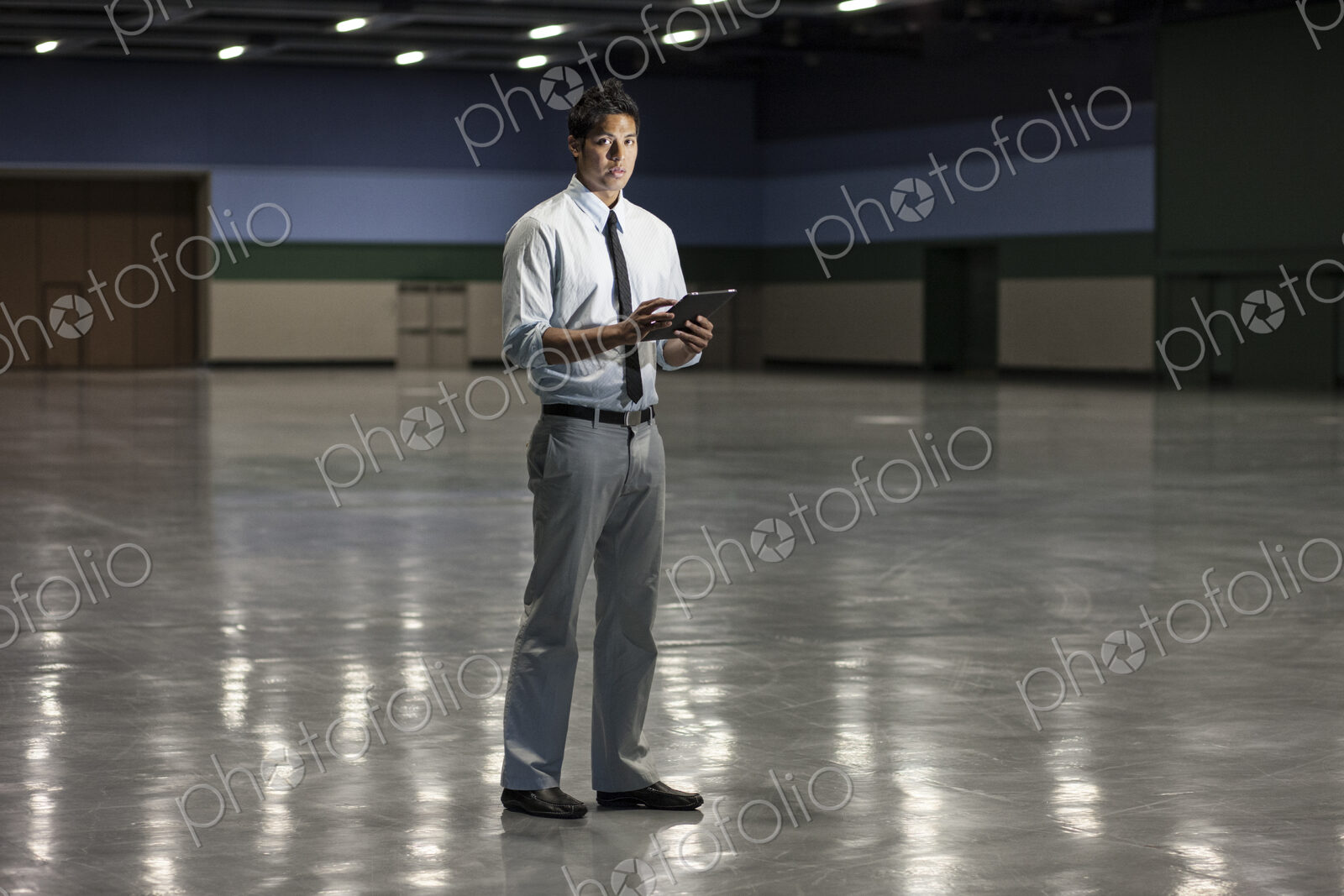 Portrait of a businessman holding a notebook computer and standing in a dimly lit and…