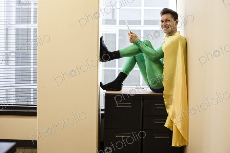 Portrait of a caucasian businessman office super hero sitting in a window using his phone.