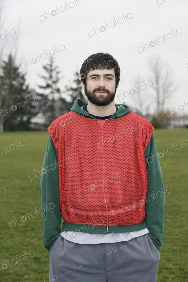 Portrait of a caucasian man playing outdoor sports, wearing a red team vest, hands in…