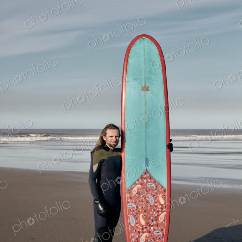 Portrait of a man holding a decorated surf board on a sandy beach Portrait of a man holding a decorated surf board on a sandy beach