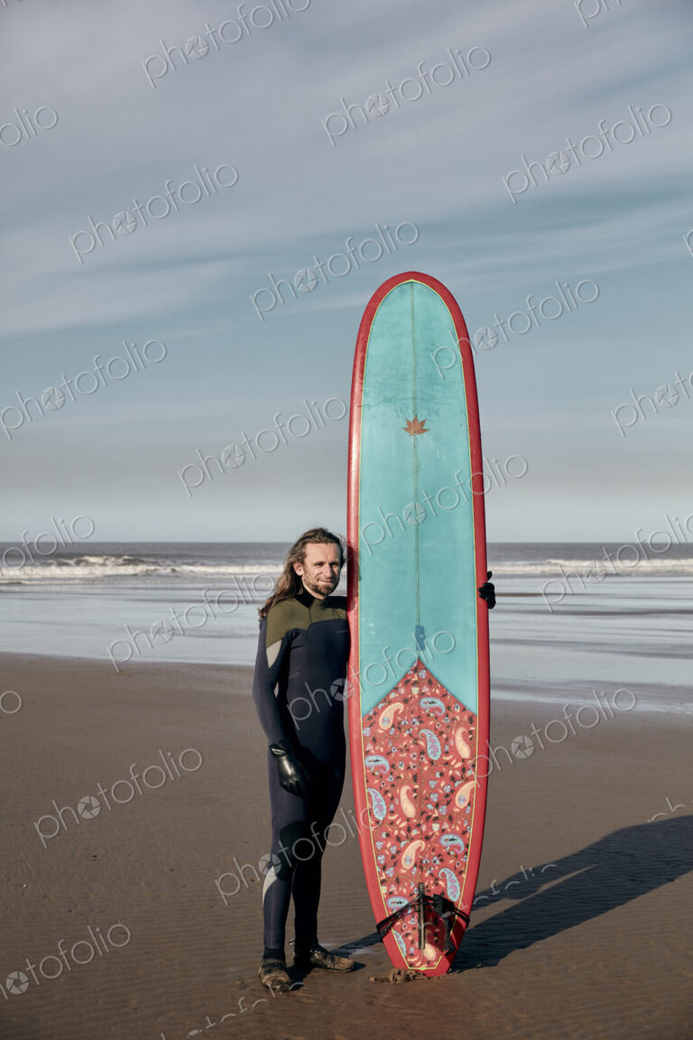 Portrait of a man holding a decorated surf board on a sandy beach