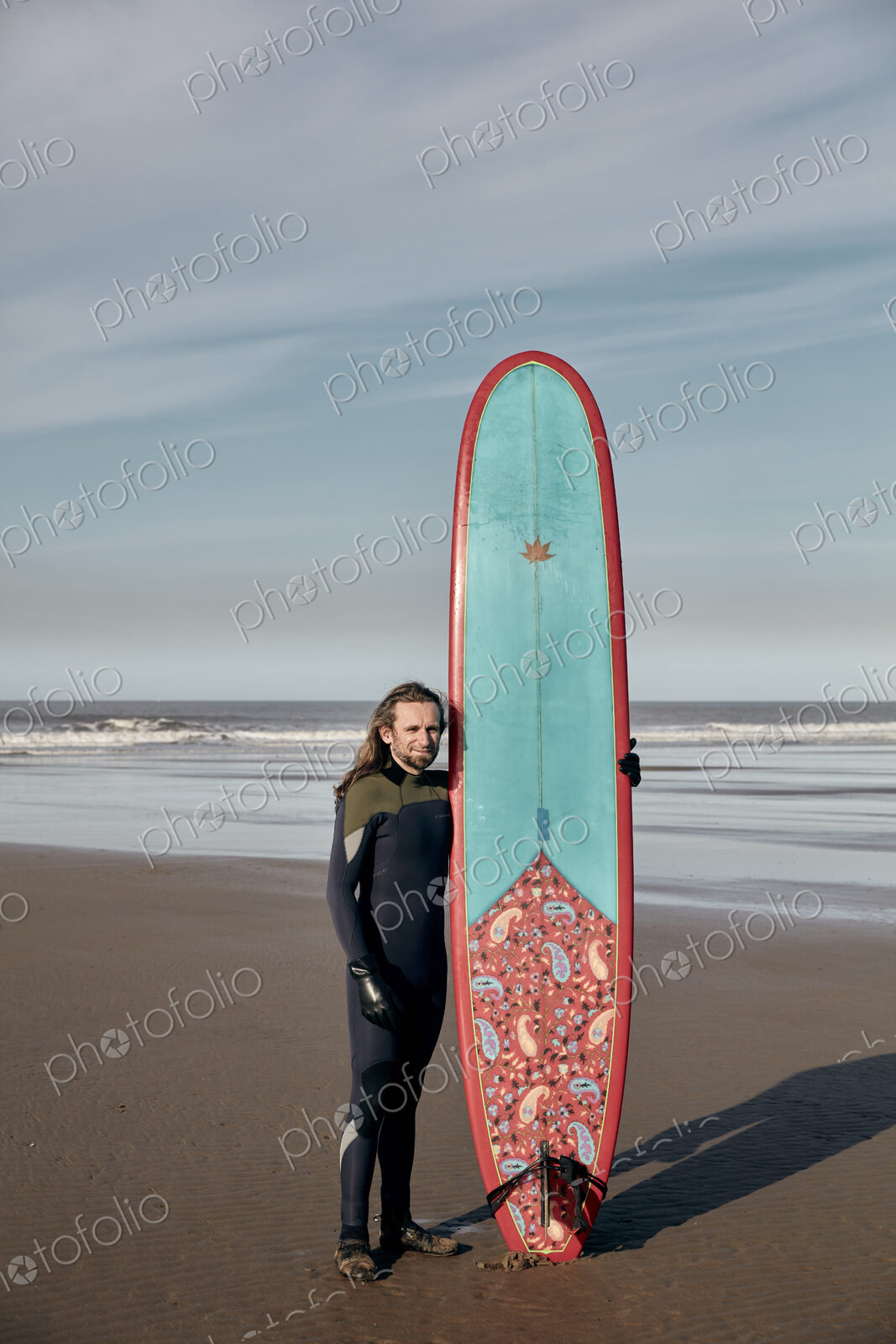Portrait of a man holding a decorated surf board on a sandy beach