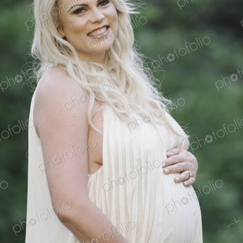 Portrait of a pregnant woman with long blond hair in a garden.