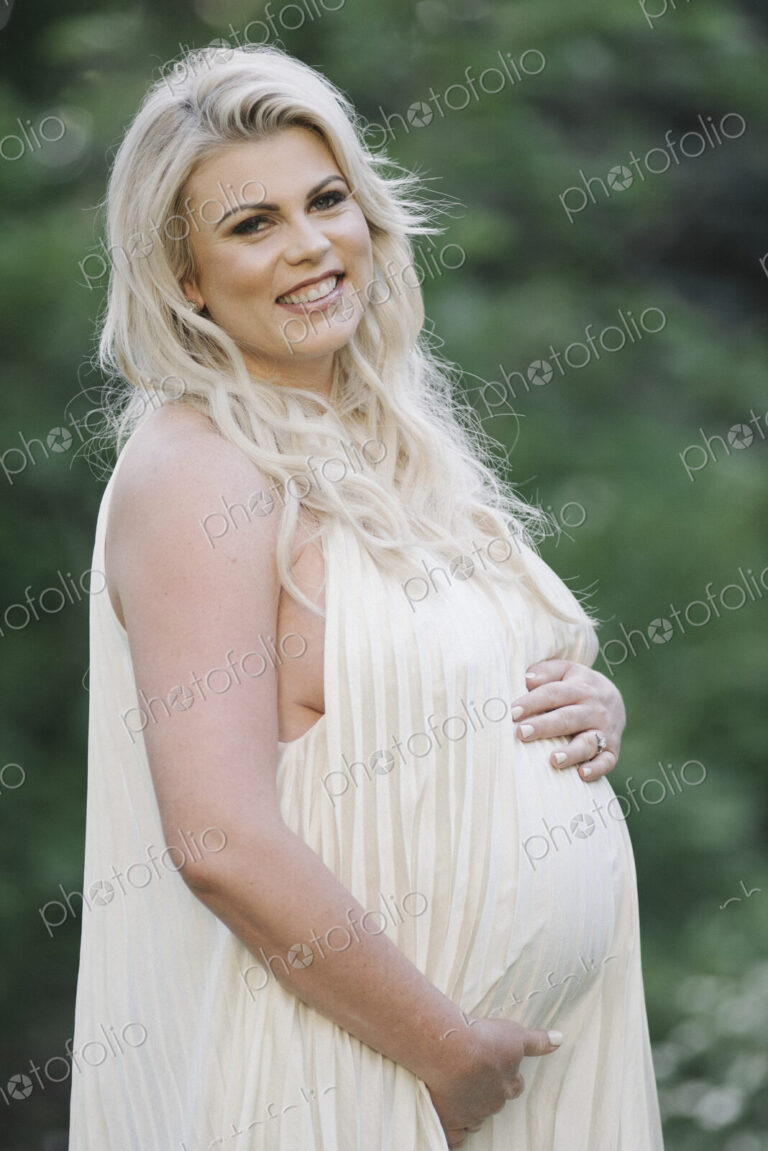 Portrait of a pregnant woman with long blond hair in a garden.
