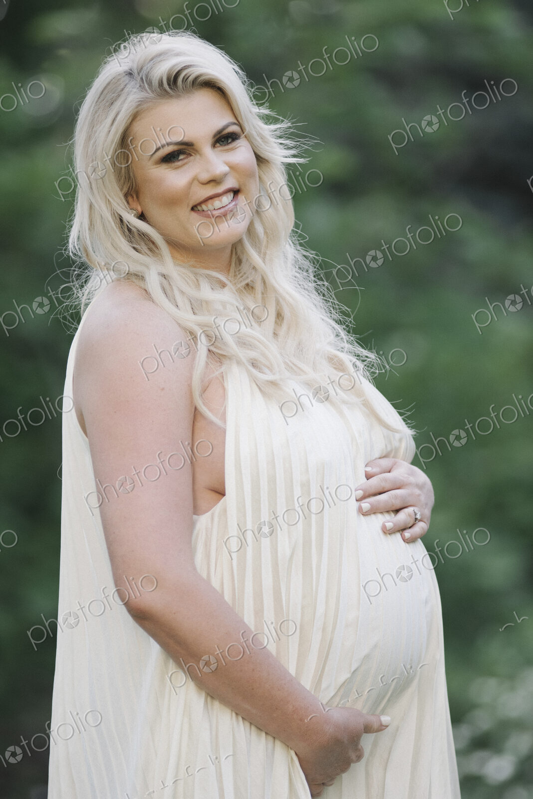 Portrait of a pregnant woman with long blond hair in a garden.