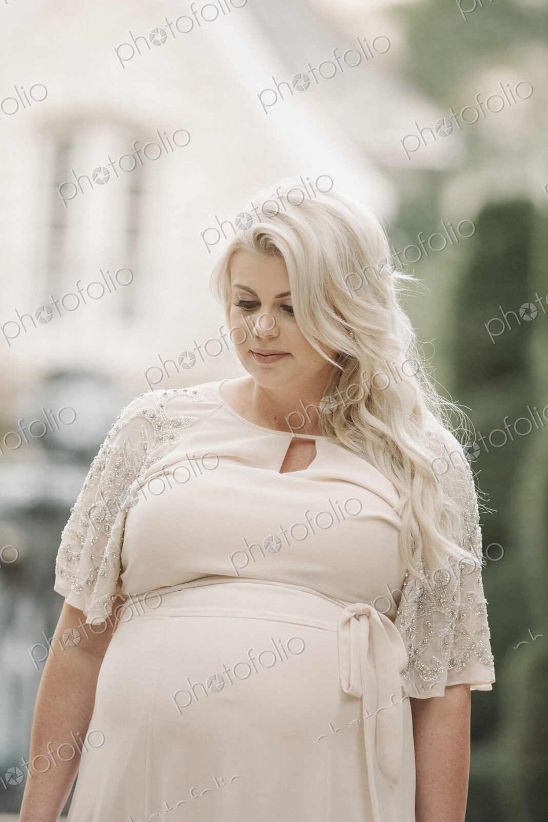 Portrait of a pregnant woman with long blond hair in a garden.