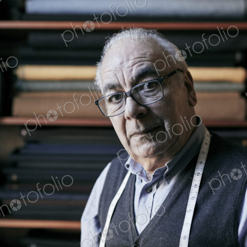 Portrait of a senior tailor with a measuring tape around his neck, in his workroom. Portrait of a senior tailor with a measuring tape around his neck, in his workroom.