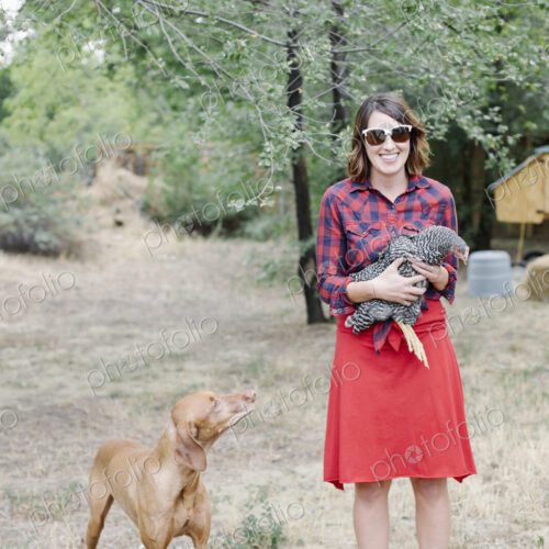 Portrait of a smiling woman holding a grey hen, a dog standing beside her. Portrait of a smiling woman holding a grey hen, a dog standing beside her.