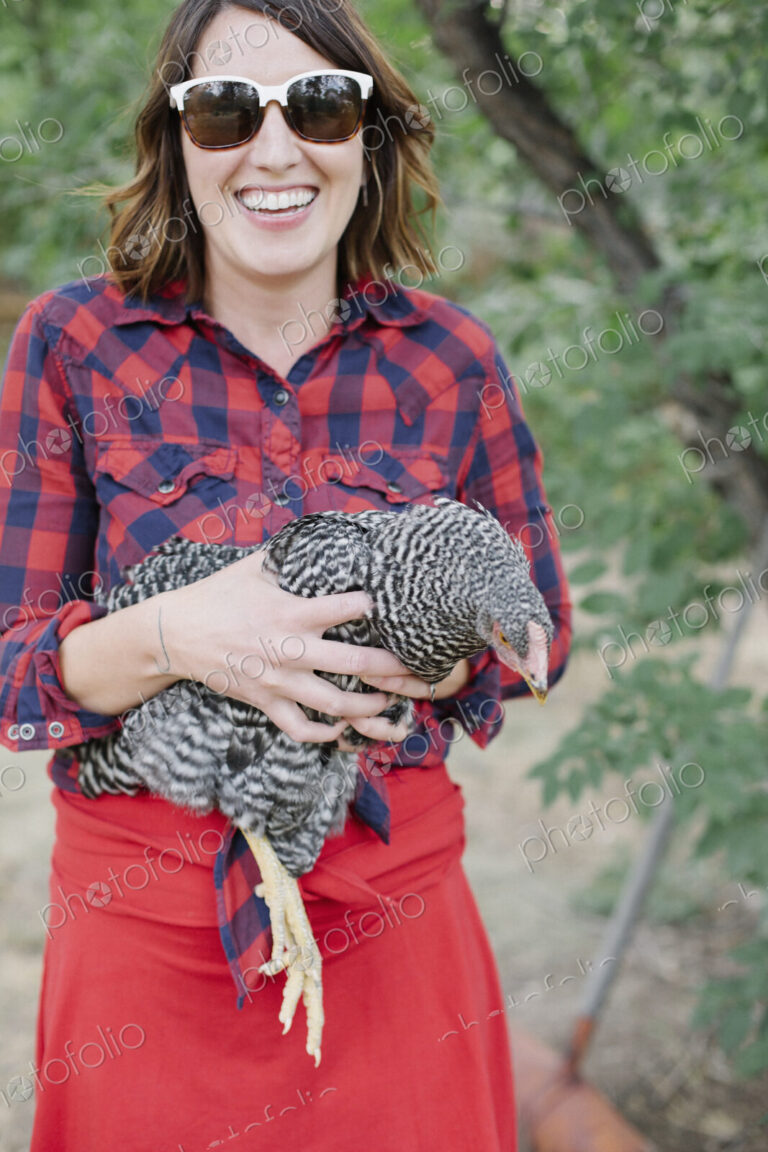 Portrait of a smiling woman holding a grey specked hen.