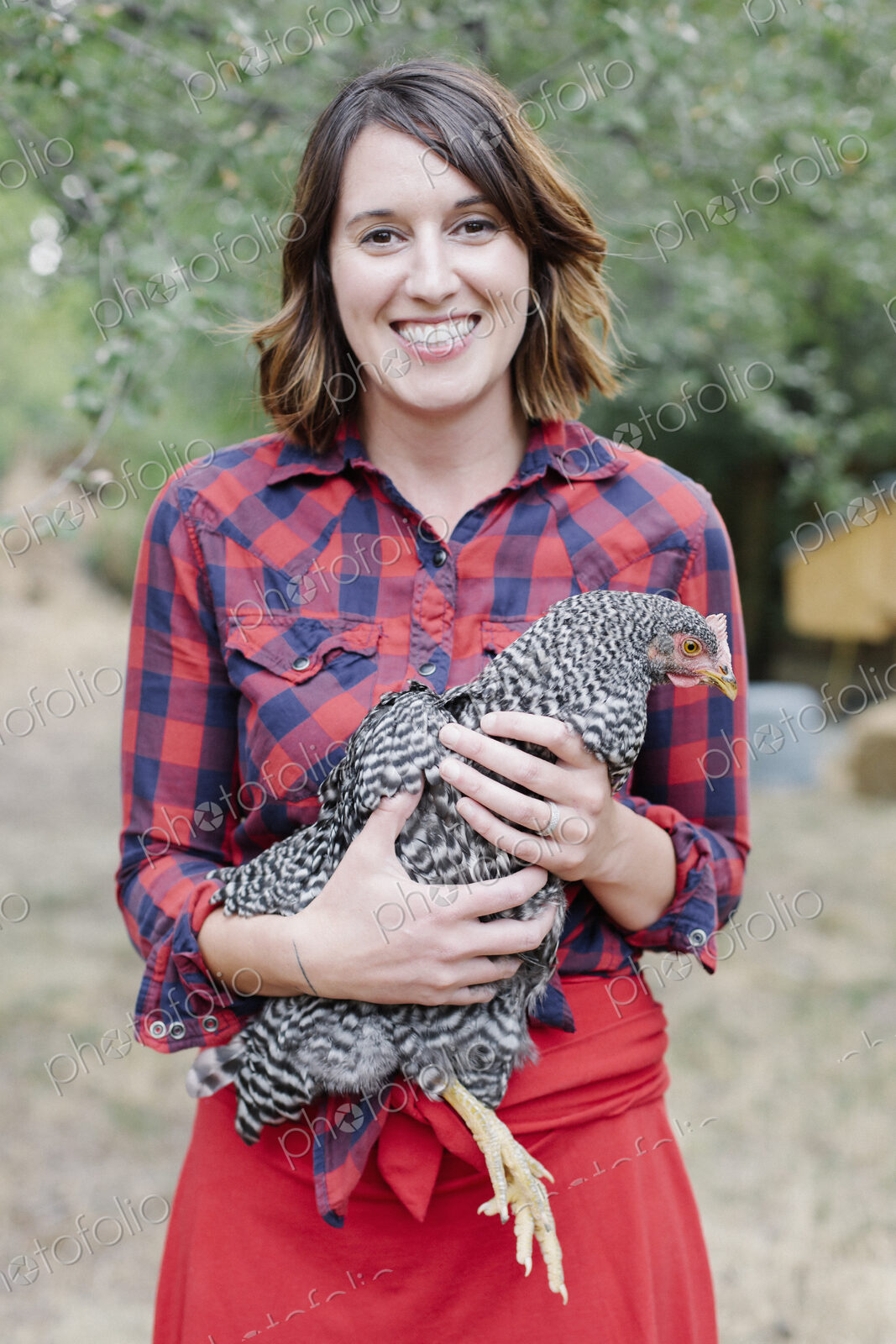 Portrait of a smiling woman holding a grey specked hen.