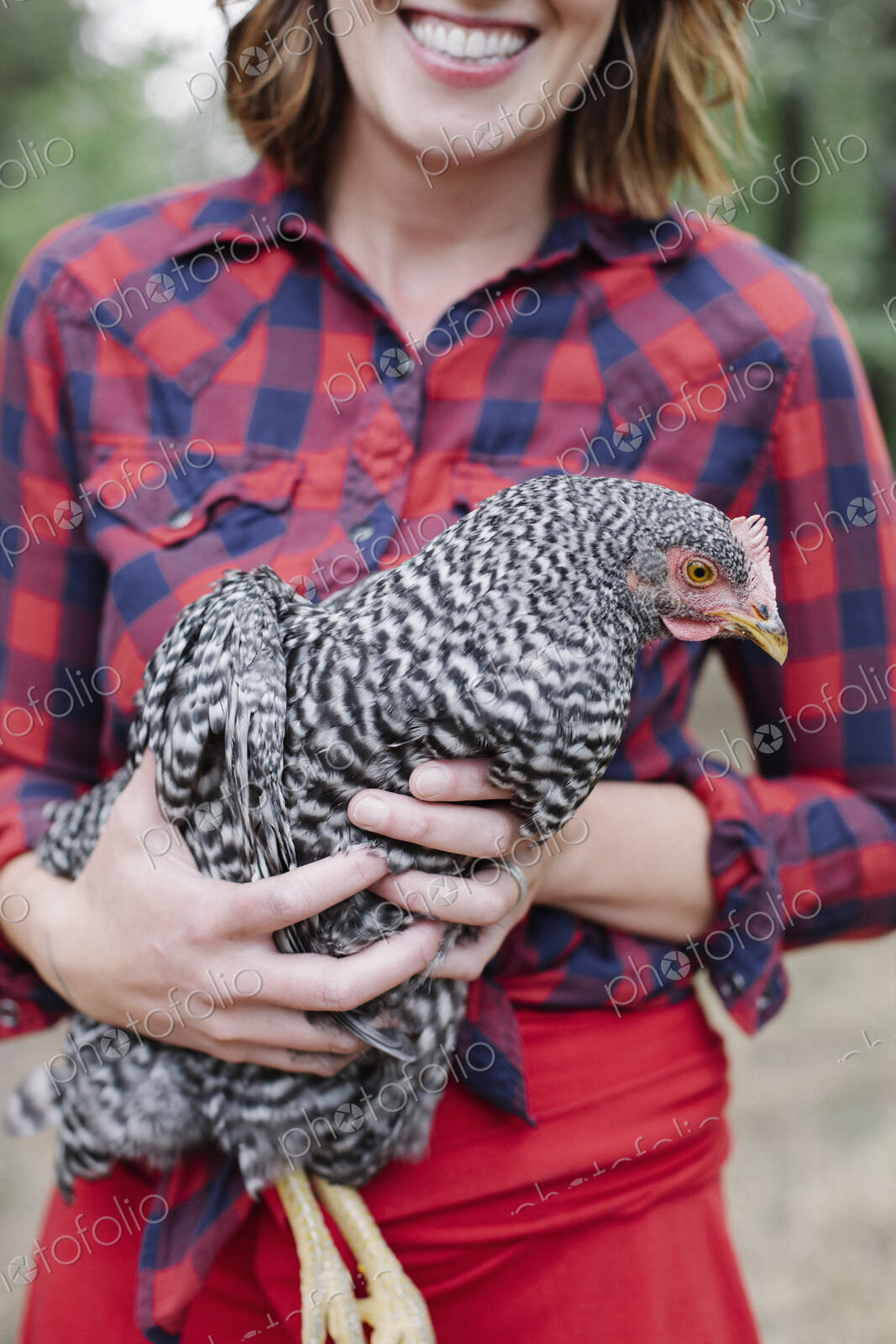 Portrait of a smiling woman holding a grey specked hen.