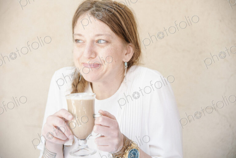 Portrait of a smiling woman with auburn hair holding a cafe latte.