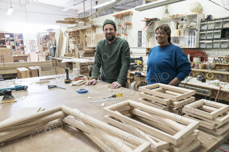 Portrait of a team of two mixed race male and female carpenters in a large woodworking…