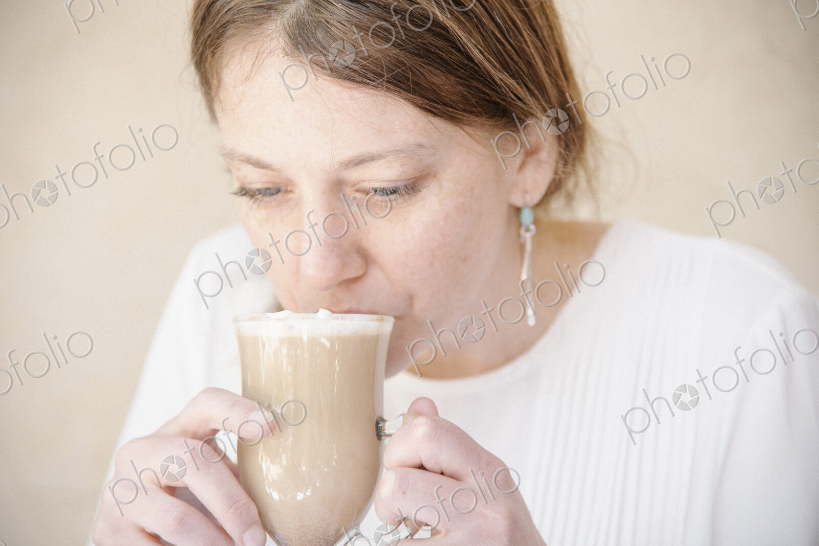 Portrait of a woman with auburn hair drinking a cafe latte.