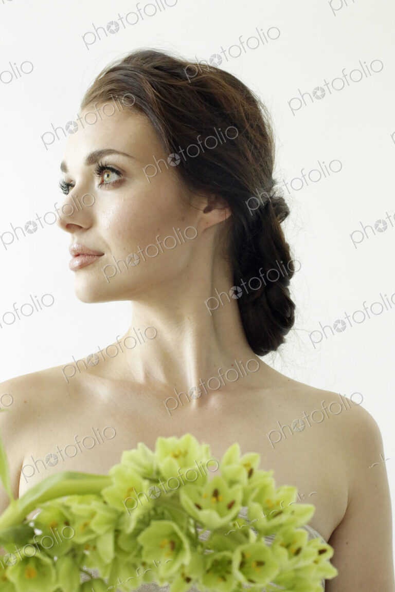 Portrait of a woman with brown hair tied in an elegant bun, wearing a dress with a…