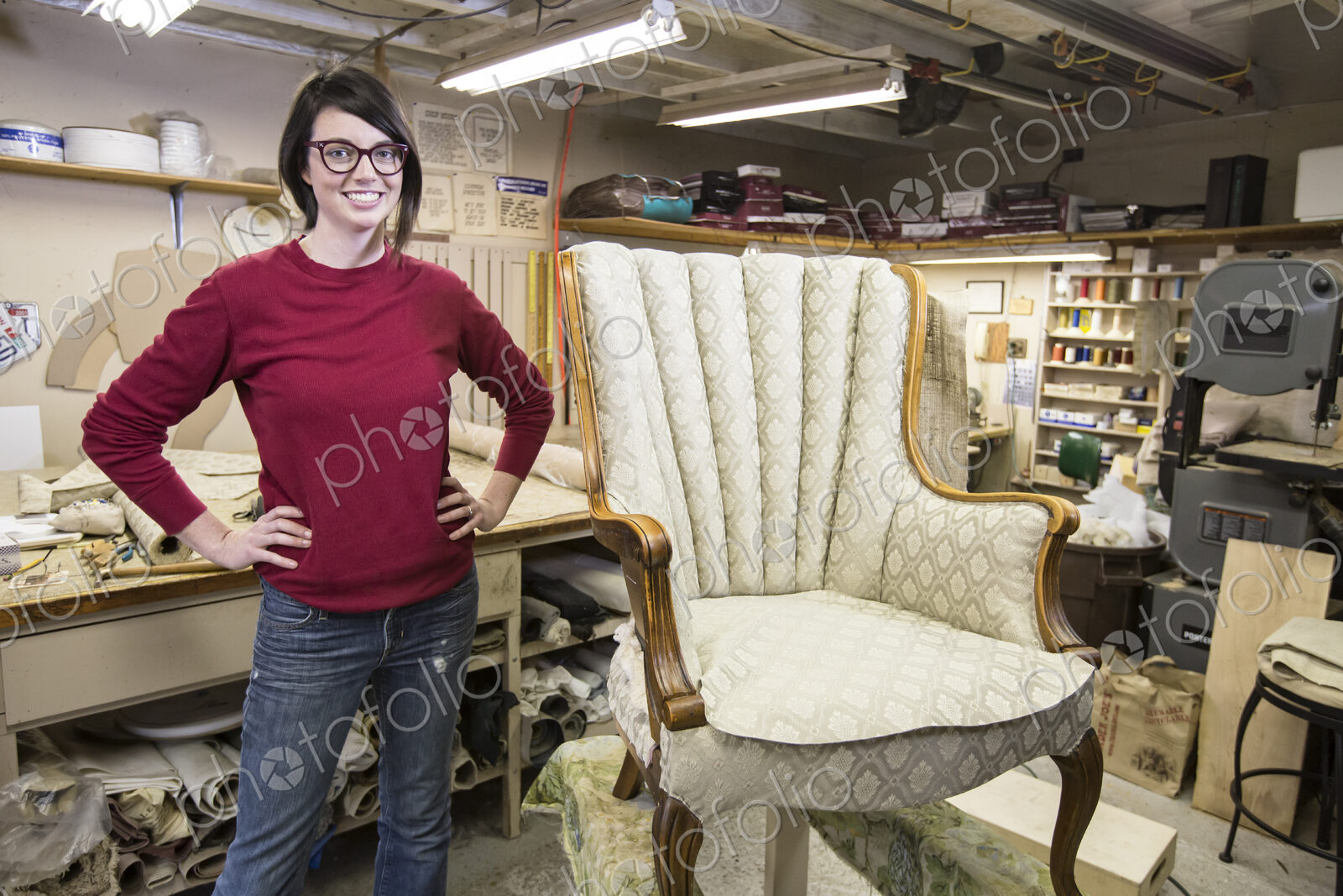 Portrait of a youg Caucasian woman upholsterer and a chair she is working on.