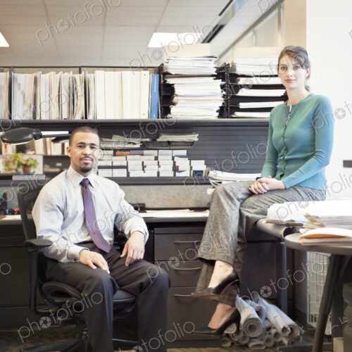 Portrait of a young Black businessman and Caucasian businesswoman in an office cubicle.