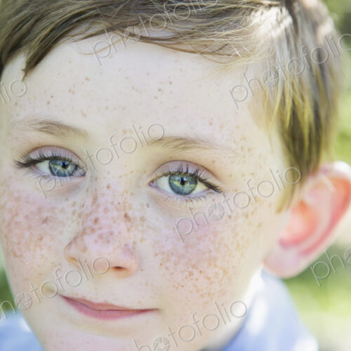 Portrait of a young boy with red hair, blue eyes and freckles on his nose.