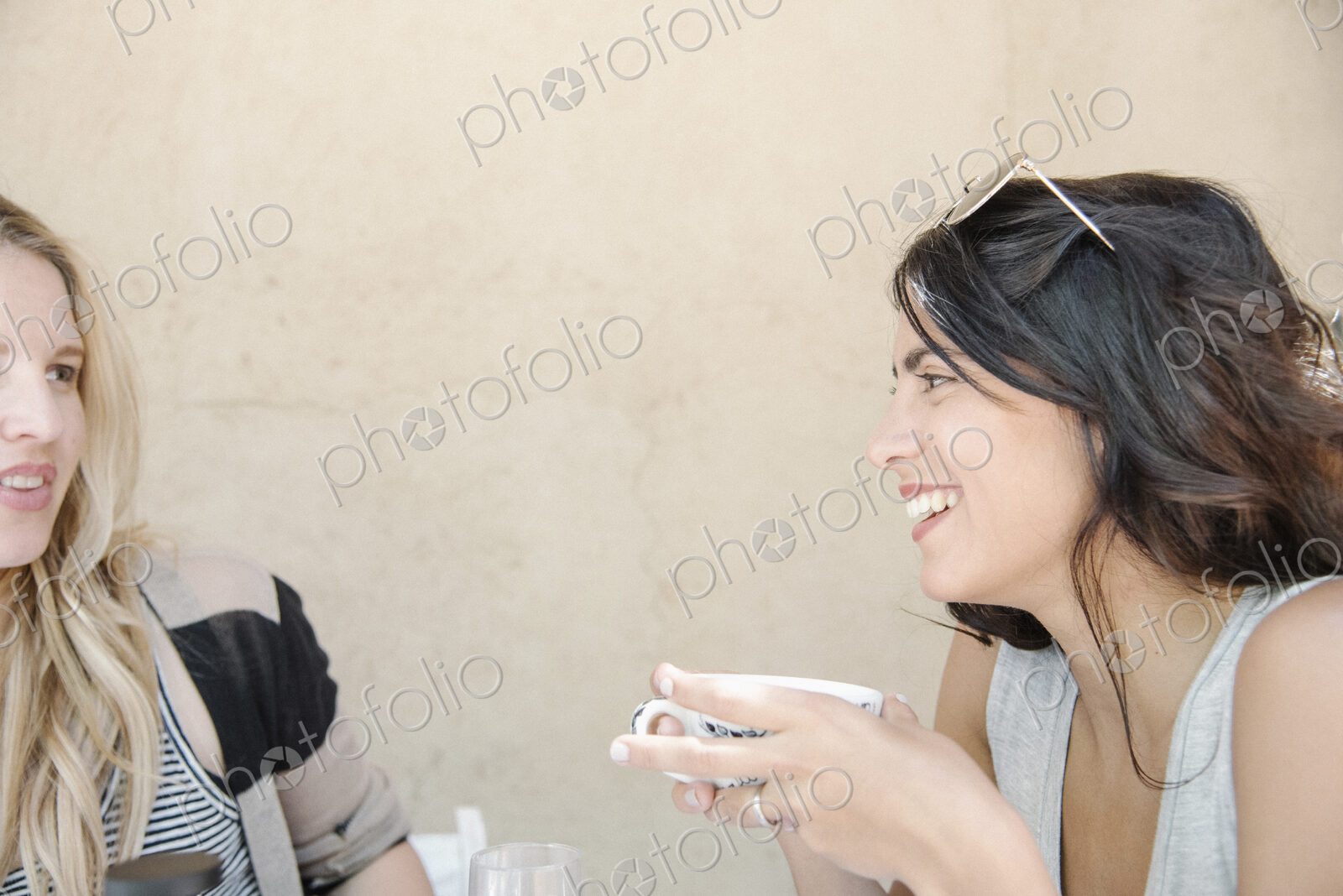 Portrait of a young woman with long brown hair holding a cup, chatting to a friend.