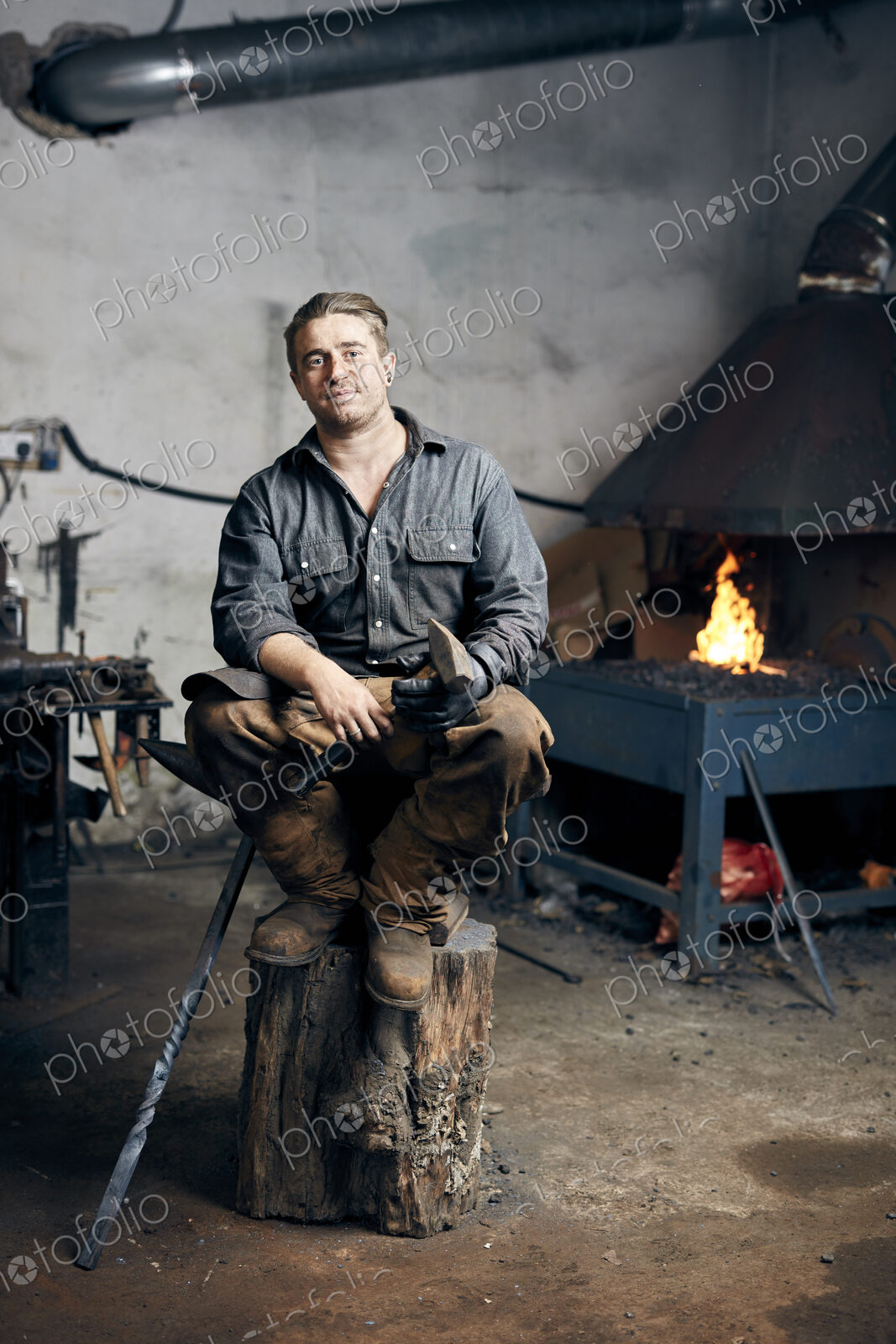 Portrait of an artisan metalworker in his workshop, sitting on a wood block holding a…