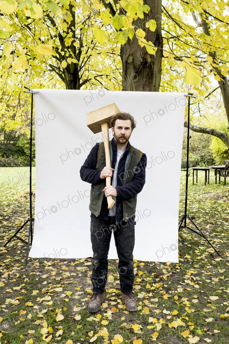 Portrait of bearded man holding wooden block standing in front of white background in…
