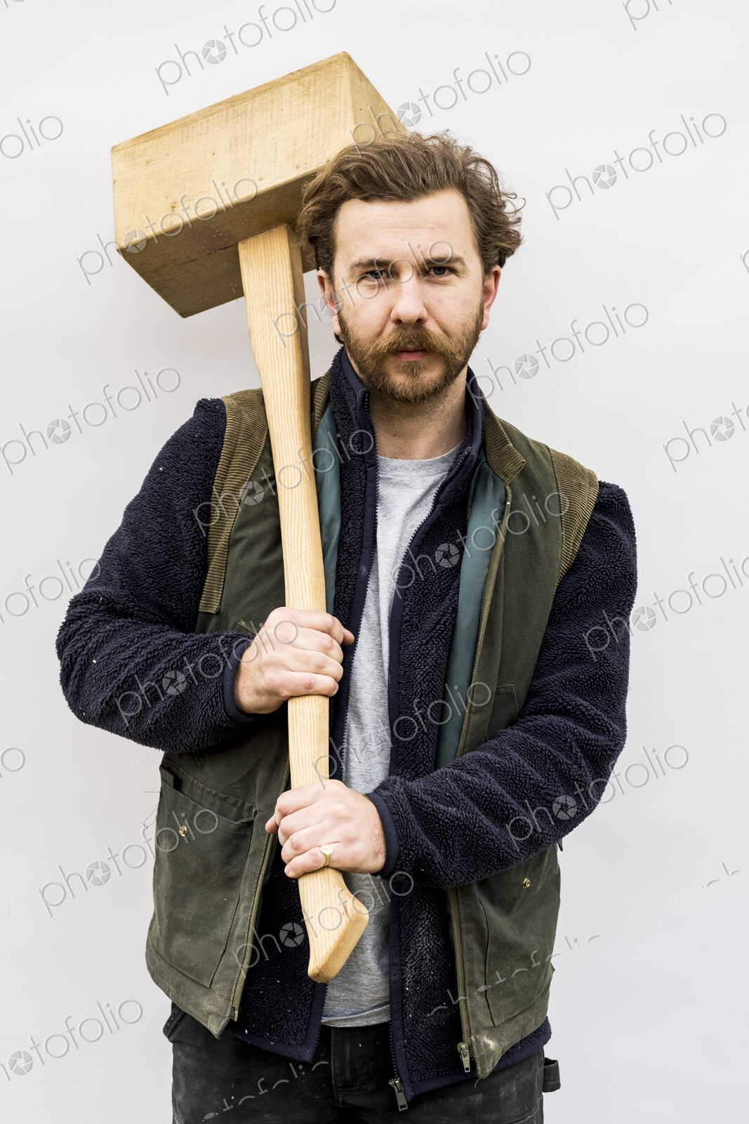 Portrait of bearded man holding wooden block standing in front of white background,…