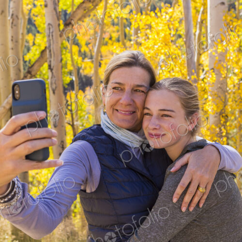 Portrait of mother and her 13 year old daughter with autumn aspens in background,…