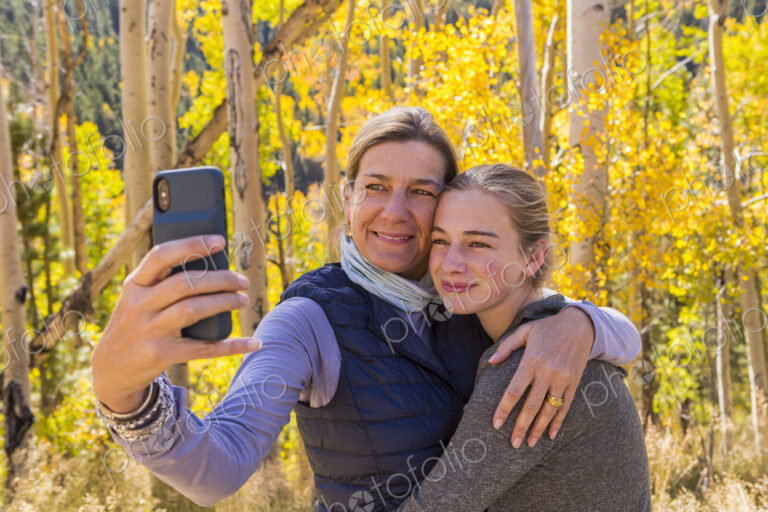 Portrait of mother and her 13 year old daughter with autumn aspens in background,…