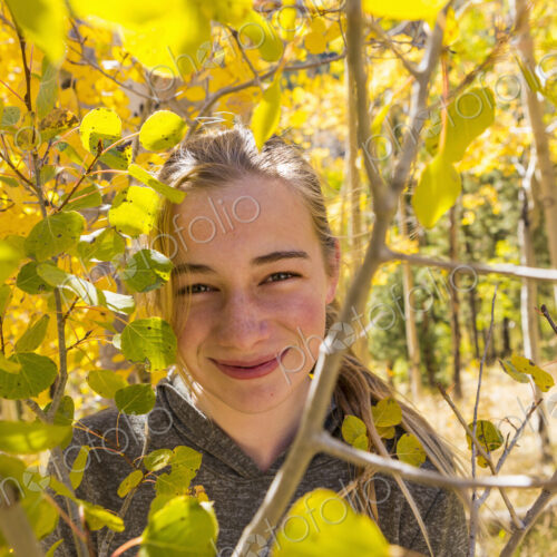 Portrait of smiling 13 year old girl hiding behind autumn aspen leaves Portrait of smiling 13 year old girl hiding behind autumn aspen leaves
