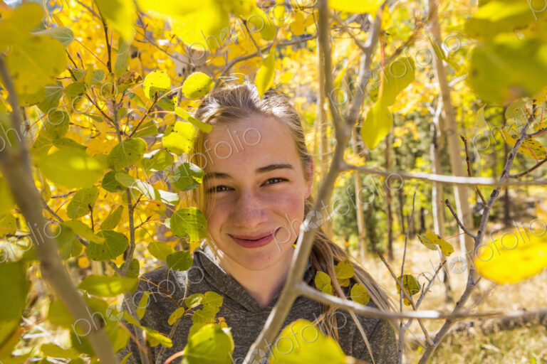 Portrait of smiling 13 year old girl hiding behind autumn aspen leaves