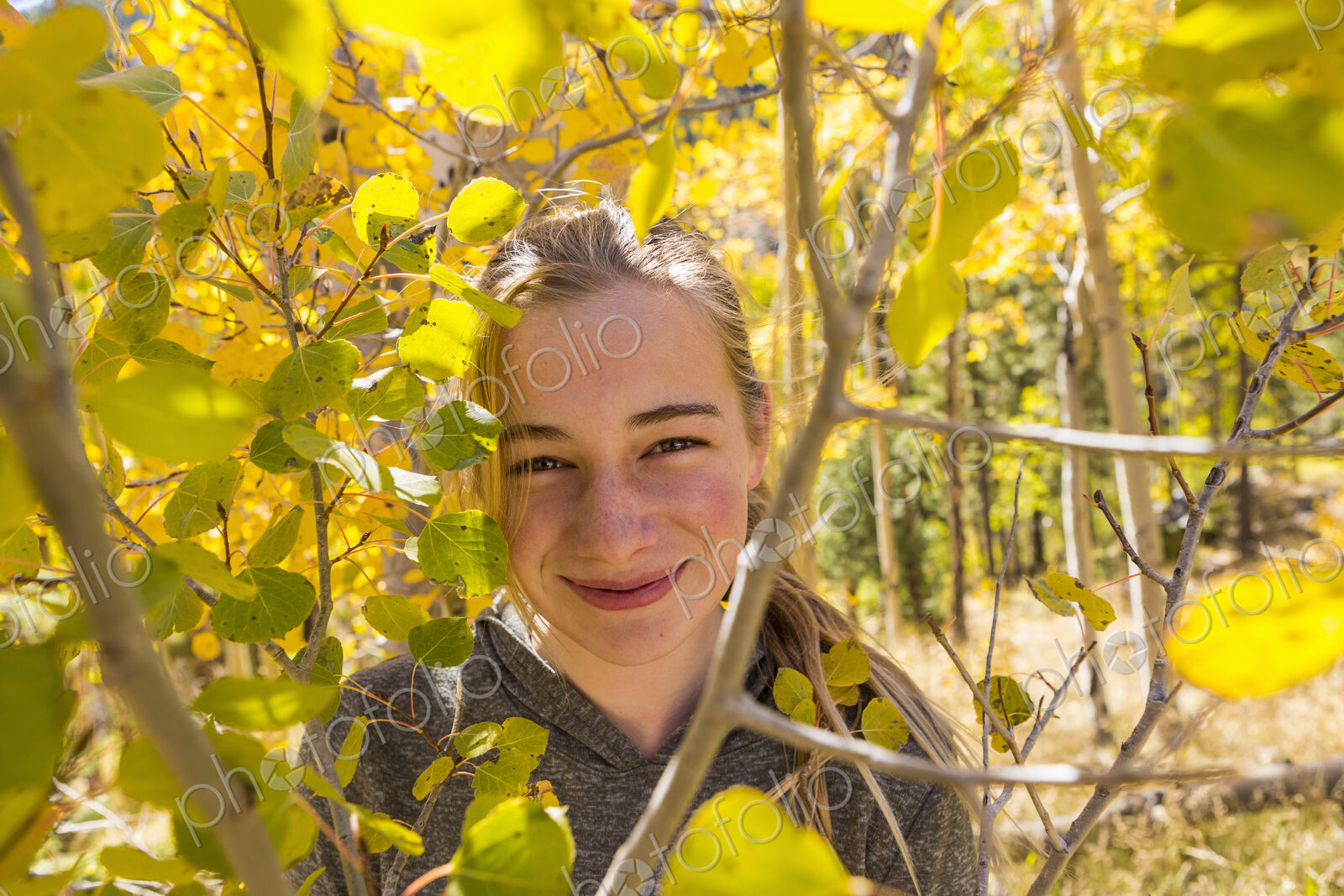 Portrait of smiling 13 year old girl hiding behind autumn aspen leaves