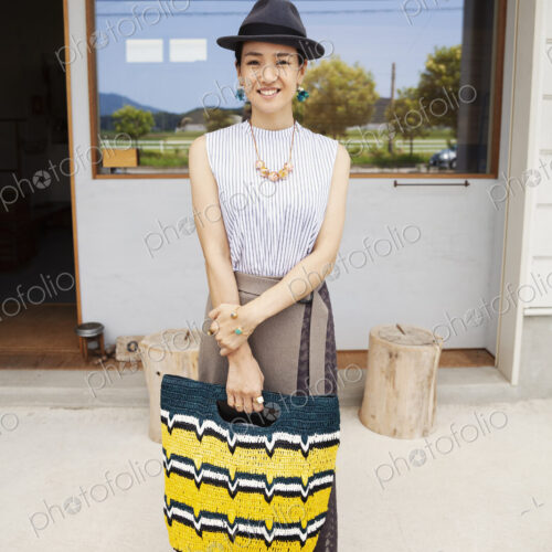 Portrait of smiling Japanese woman wearing hat and holding shopping bag, looking at… Portrait of smiling Japanese woman wearing hat and holding shopping bag, looking at…