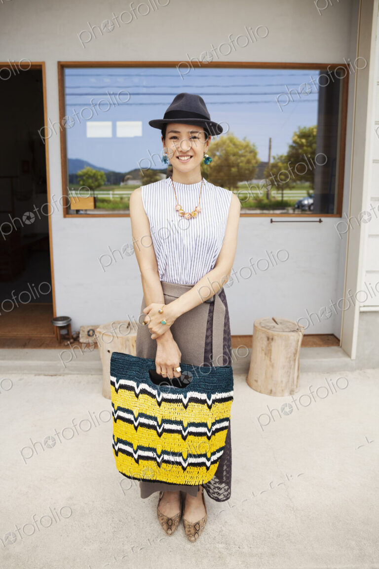 Portrait of smiling Japanese woman wearing hat and holding shopping bag, looking at…