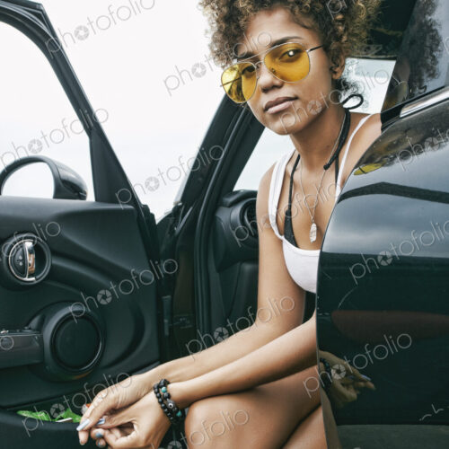 Portrait of smiling young woman sitting in car in sunglasses looking at camera.