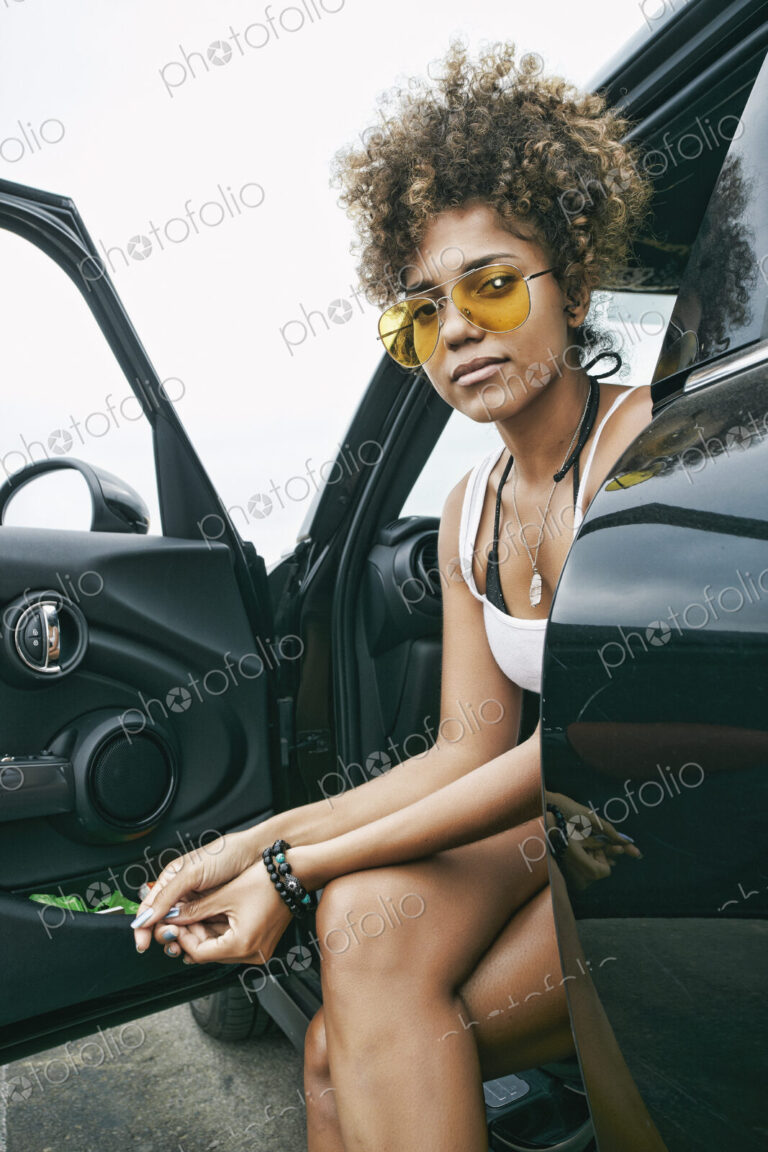 Portrait of smiling young woman sitting in car in sunglasses looking at camera.
