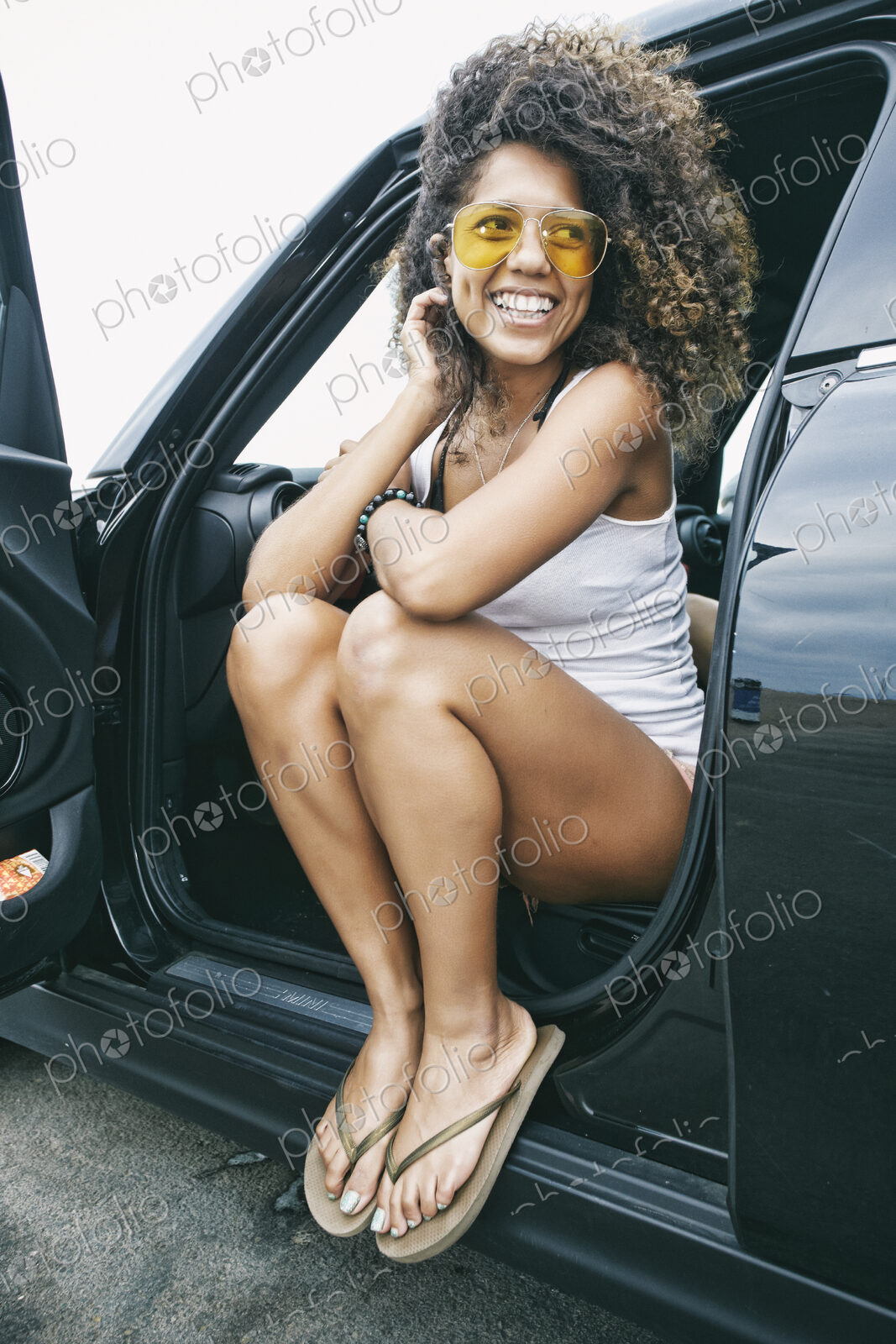 Portrait of smiling young woman wearing sunglasses, white vest and flip flops.